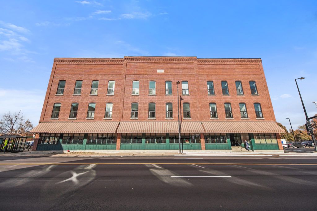 A large brick building with multiple windows, situated alongside a street under a clear blue sky.