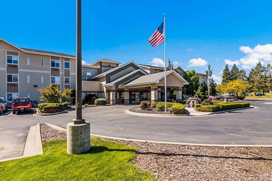 Exterior view of a hotel entrance with a flag and landscaped surroundings.