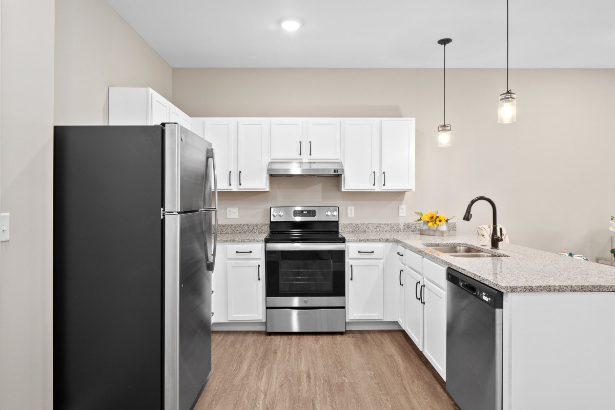 A modern kitchen with white cabinetry and stainless steel appliances, featuring a refrigerator, oven, and dishwasher.