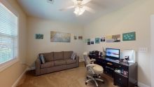A cozy home office with a couch, desk, and computer setup surrounded by wall art.