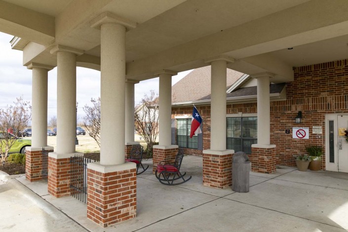 A covered patio with brick columns features rocking chairs and a Texas flag.