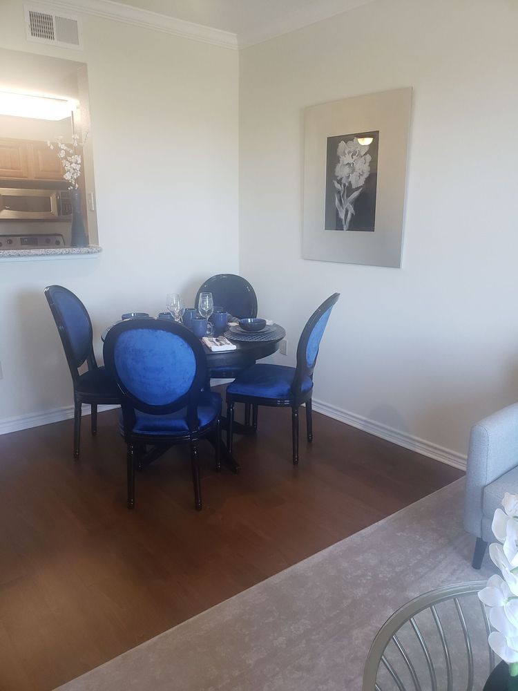 A cozy dining area with a round table and blue chairs, complemented by artwork on the wall and a hardwood floor.