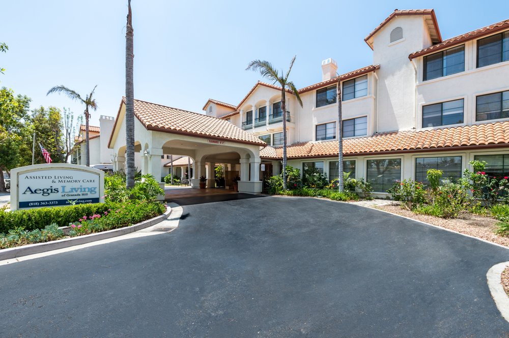 A Mediterranean-style building with a covered entrance and palm-lined driveway.