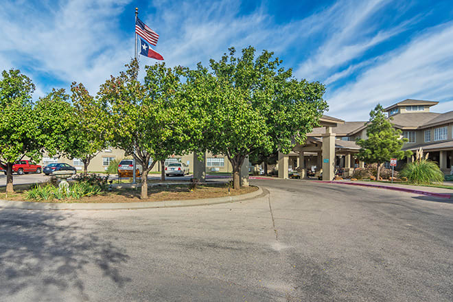 A building entrance with trees and flags under a blue sky.