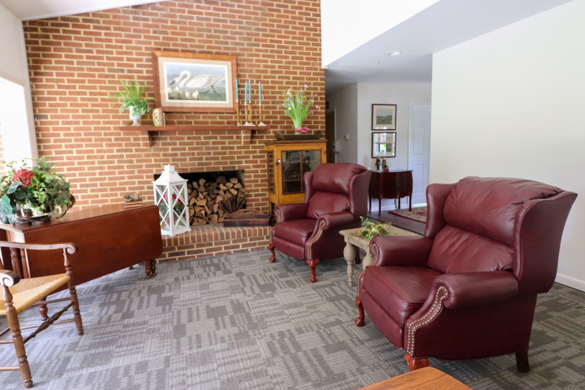 A cozy living room featuring a brick fireplace, leather armchairs, and traditional decor.