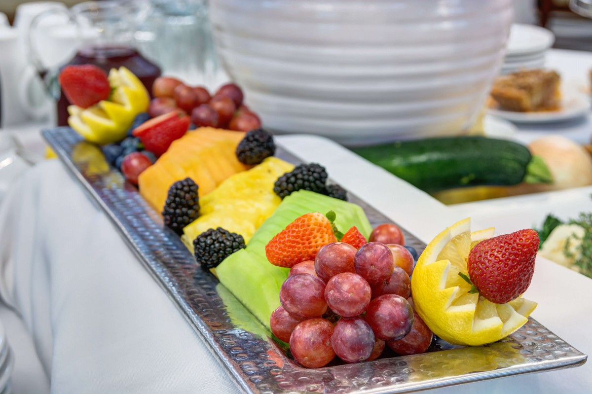 A colorful fruit platter featuring an assortment of fresh fruits including grapes, melon, strawberries, pineapple, and blackberries, garnished with a lemon slice.