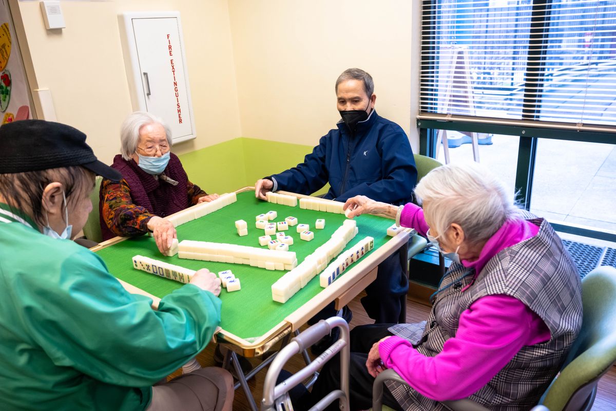 A group of seniors playing mahjong together in a community setting.