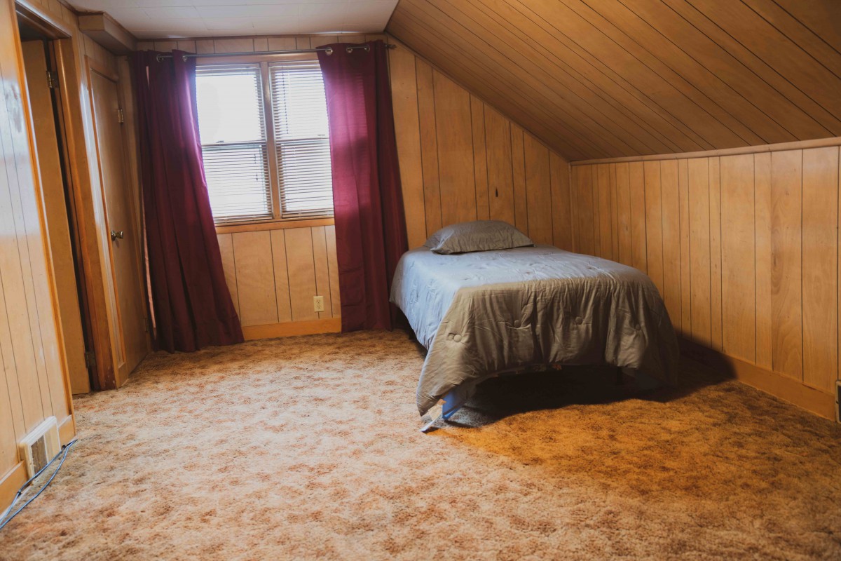 A cozy attic bedroom with wood paneling, a single bed, and purple curtains.