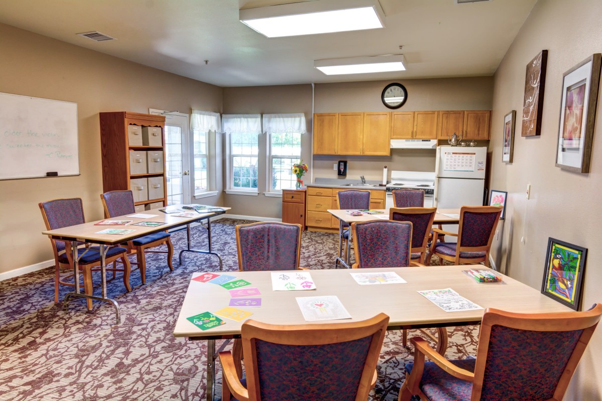 A well-lit office space with tables and chairs, featuring a kitchenette along one wall.