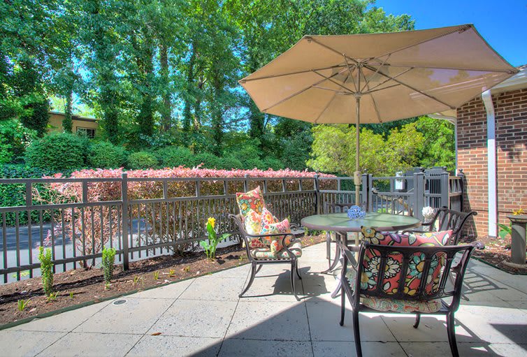 A sunny patio area with outdoor furniture and an umbrella, surrounded by lush greenery.