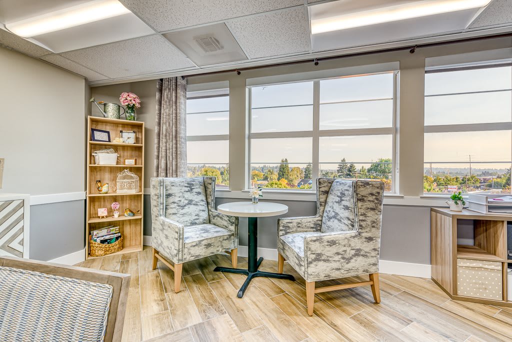 A cozy seating area with two patterned chairs and a small round table near large windows.