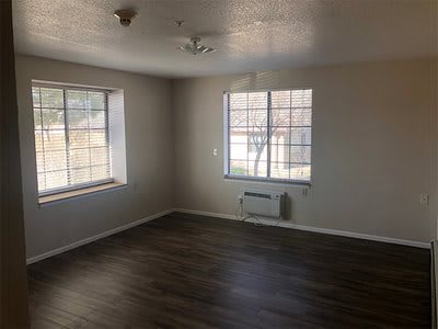 An empty room with hardwood flooring and large windows.