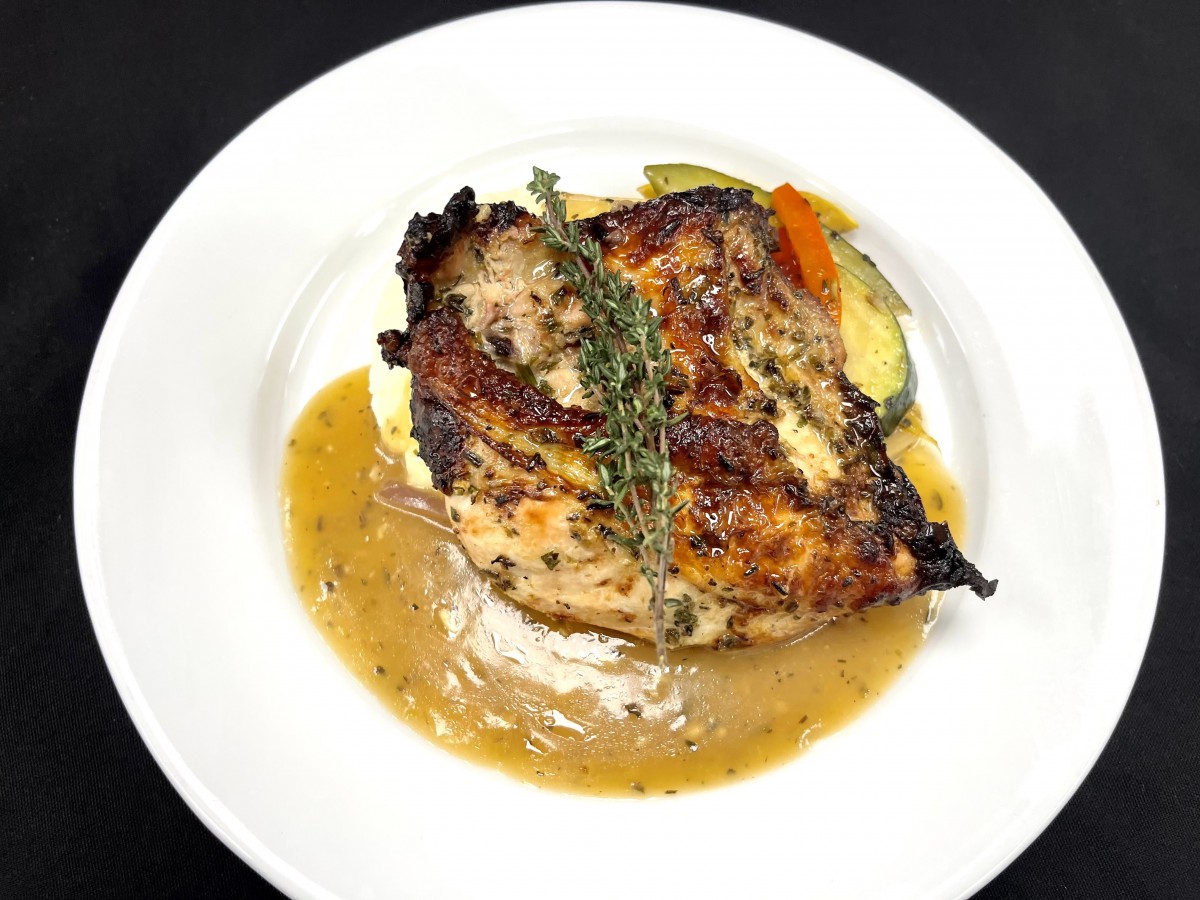 A delicious plate of roasted chicken served with sauce and vegetables, garnished with herbs.