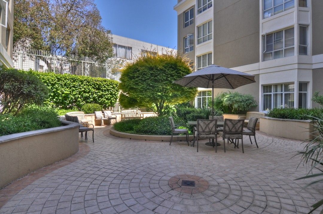 A peaceful courtyard featuring outdoor seating, greenery, and an umbrella for shade.