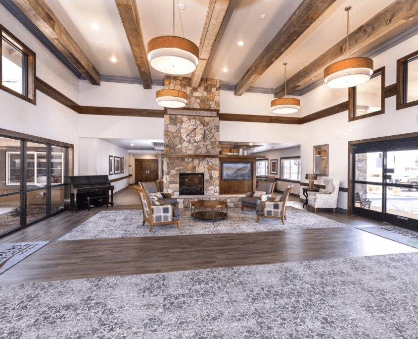 A spacious and modern living room featuring a central stone fireplace, wooden ceiling beams, and comfortable seating.