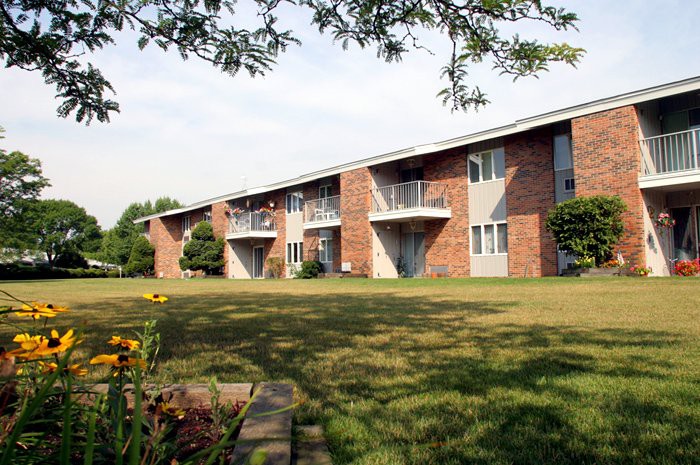A brick apartment building with balconies and a grassy lawn in the foreground.
