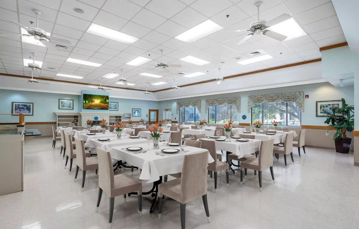 A spacious and elegantly set dining area with multiple tables and chairs, featuring large windows and ceiling lights.