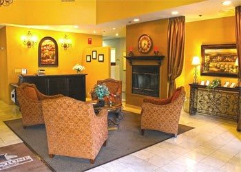 A cozy hotel lobby featuring comfortable seating around a central fireplace with warm color tones.