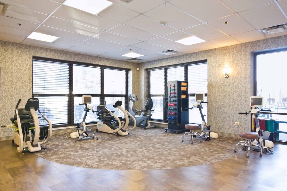 A well-lit rehabilitation room with stationary bikes and large windows.