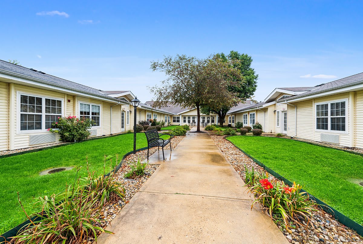 A landscaped pathway with benches leads through a garden area between residential buildings.