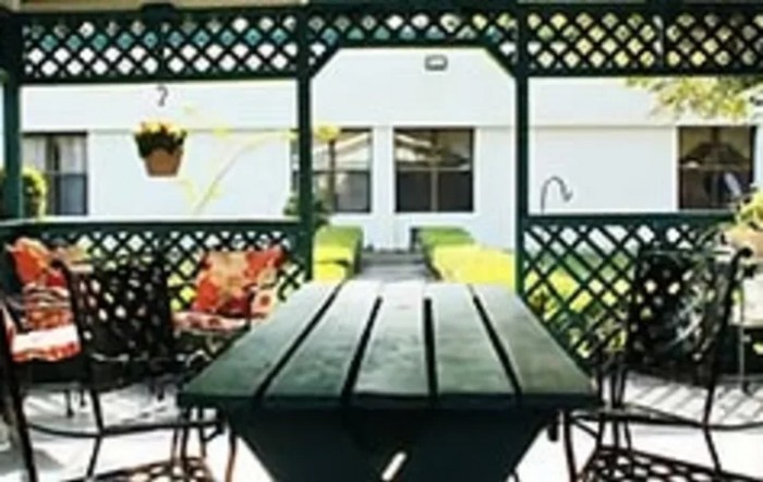An outdoor patio area featuring a long wooden table, surrounded by chairs and lattice fencing with hanging plants.