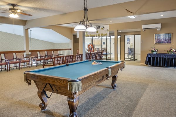 A well-lit game room featuring a classic pool table and comfortable seating.