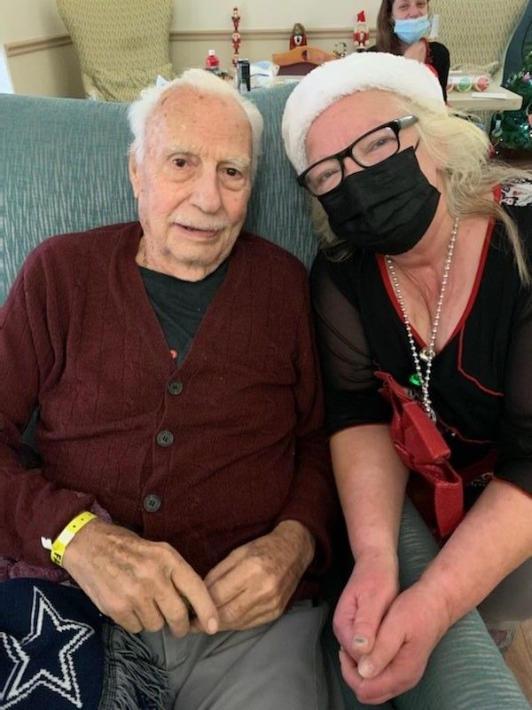 An elderly man and a woman wearing a mask sit together indoors.