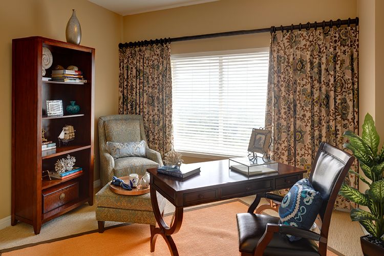 A cozy home office with a desk, armchair, and bookshelf by a window.
