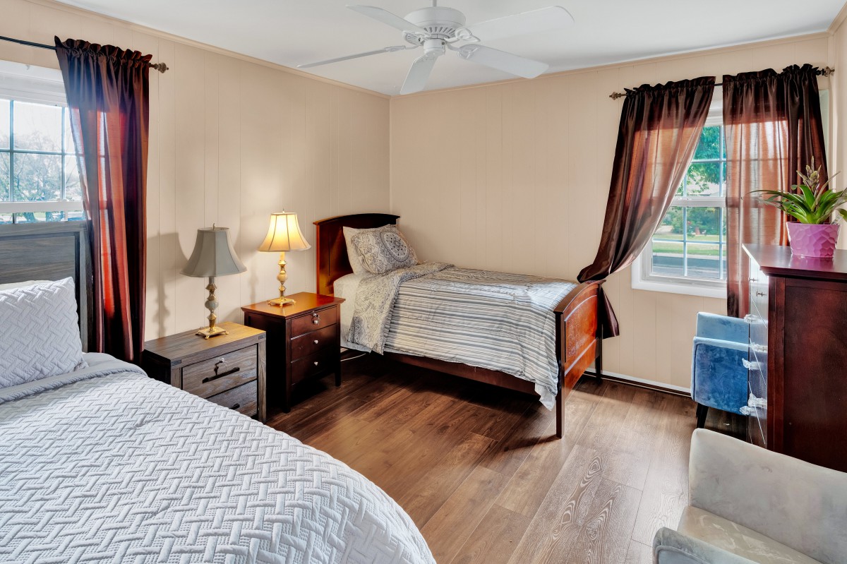 A cozy bedroom featuring two twin beds, a nightstand with a lamp, and a window with curtains.