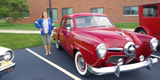 A woman stands next to a beautiful red classic car, showcasing the charm of vintage automobiles.