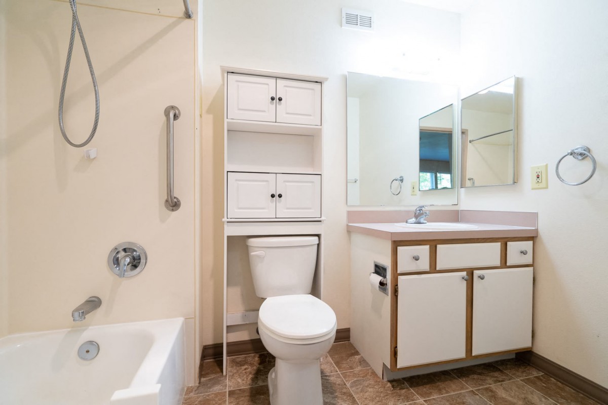 A clean and bright bathroom with a toilet, vanity, mirror, and bathtub.