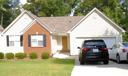 A suburban house with a brick facade and a car parked in the driveway.