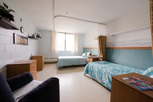 A well-lit dormitory room featuring two neatly made beds, a desk, and ample storage space.