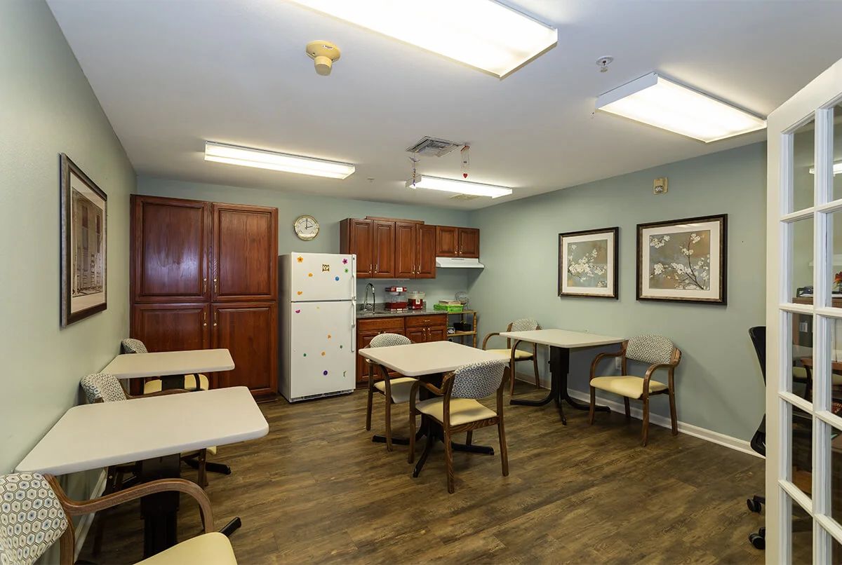 A communal kitchen and dining area with tables, chairs, refrigerator, and cabinets.