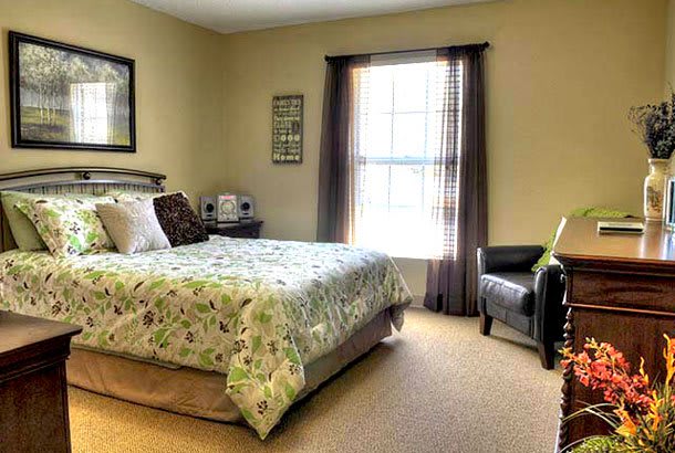 A cozy bedroom with a bed, chair, and large window letting in natural light.