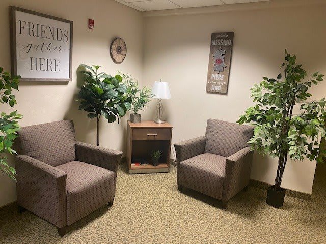 A cozy office waiting area with two chairs, indoor plants, and decorative wall art.
