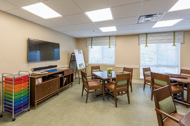 A well-lit conference room with a table, chairs, a television, and windows.