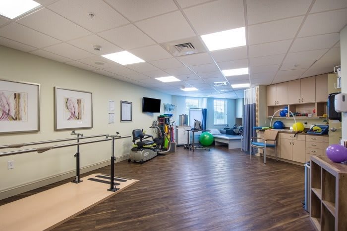 A spacious rehabilitation room equipped with various exercise machines and parallel bars for physical therapy.