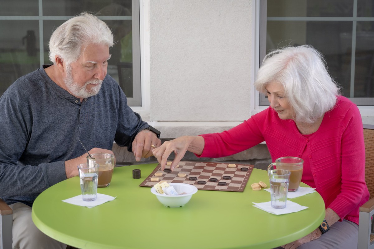 An elderly couple enjoying a game of checkers together outdoors.