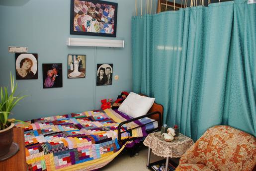 A cozy bedroom with a colorful patchwork quilt, adorned with photos on the walls and light blue curtains.