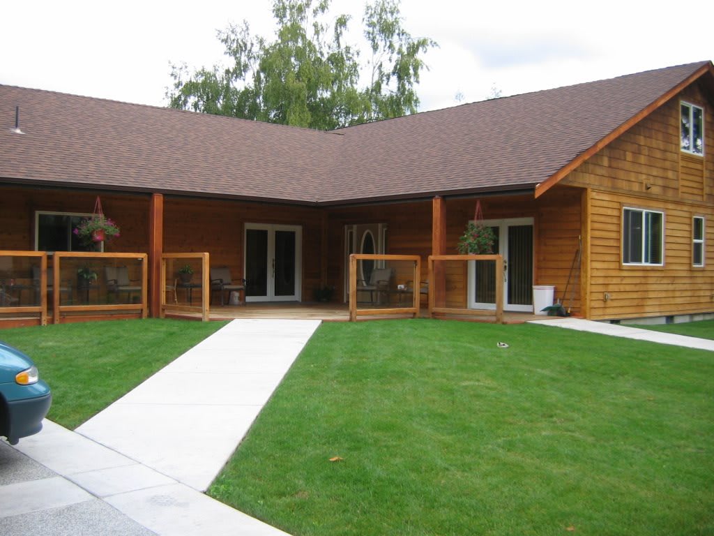 A charming wooden house with a lush green lawn and a concrete pathway leading to the entrance.
