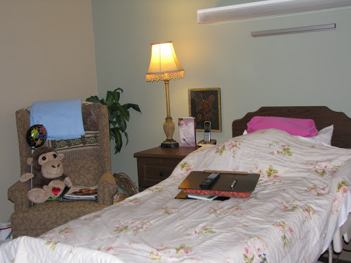 A cozy bedroom setup featuring a bed with floral bedding, a bedside lamp, and a comfortable chair.