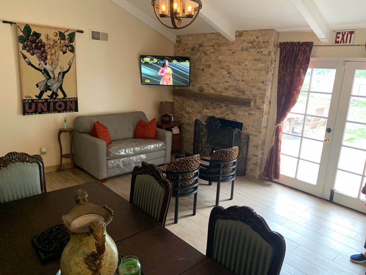 A cozy living room featuring a stone fireplace, wall-mounted TV, and dining area with chairs.