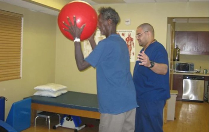 A person engaging in a physical therapy session with an instructor using an exercise ball.