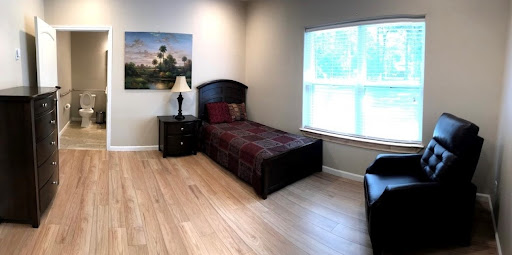 A serene and minimalist bedroom featuring a single bed, a nightstand with a lamp, and a large window that lets in natural light.