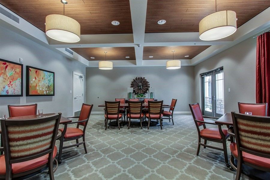 A well-lit dining room with a central table and chairs, featuring modern ceiling lights and a patterned carpet.