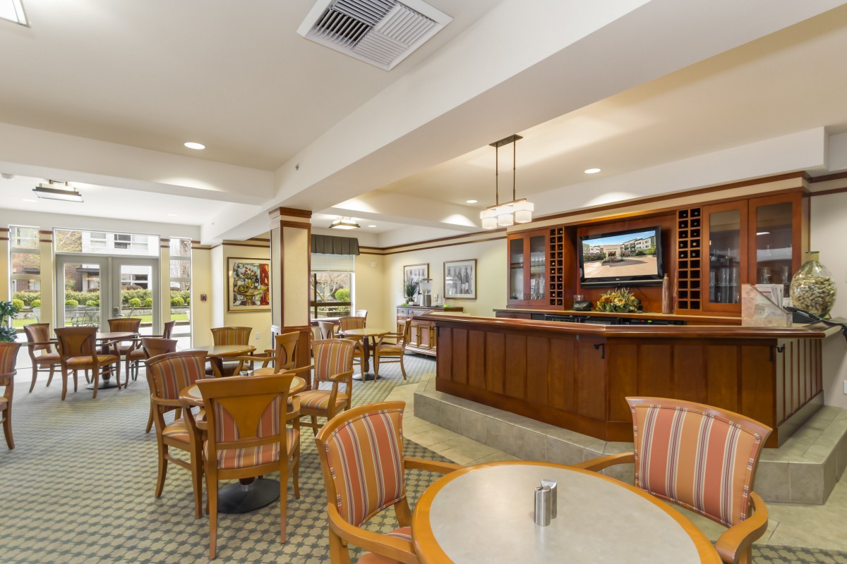 A cozy dining area with wooden tables and chairs, featuring a bar in the background.