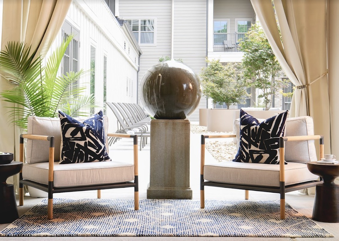 A modern outdoor seating area featuring two chairs with patterned pillows and a decorative sphere centerpiece in a courtyard setting.
