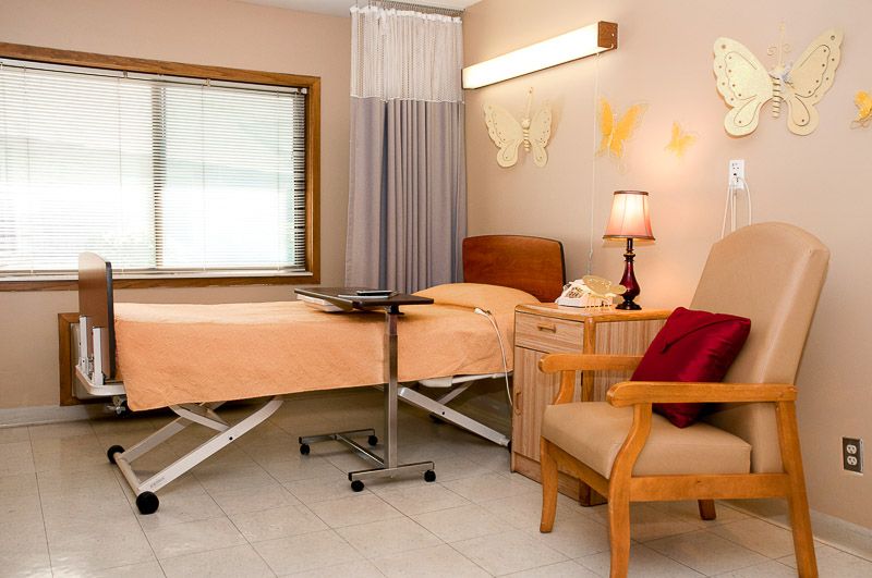 A cozy hospital room with a bed, chair, and soft lighting.