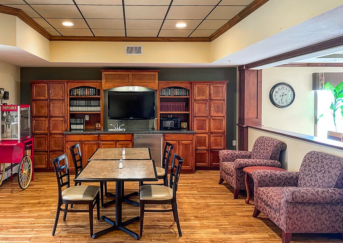 A cozy meeting room with wooden bookshelves, a central table surrounded by chairs, a television, and a clock on the wall.
